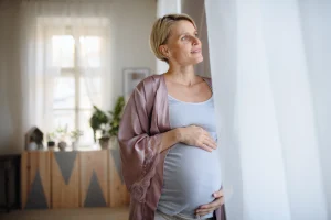 Pregnant woman standing by a window, representing age and fertility and family-building planning.